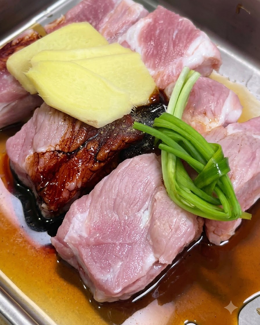 Costine di maiale marinate con fette di zenzero, cipollotti e salse in un vassoio.