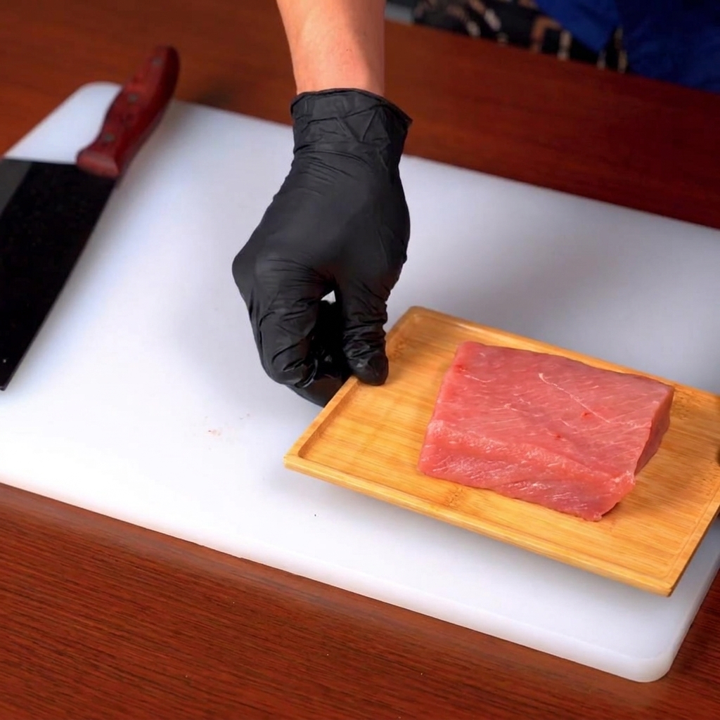 Un taglio di lombo di maiale crudo affettato su un tagliere di legno sopra una superficie bianca.