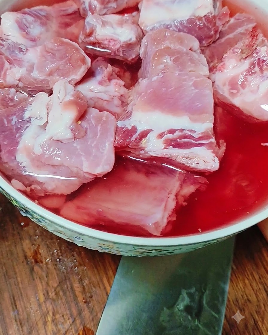 Costine di maiale crude in ammollo in una ciotola riempita di acqua tinta di rosso.