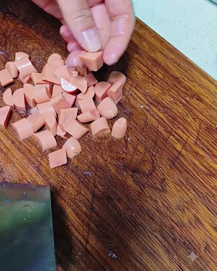 Mani che tagliano la salsiccia a piccoli pezzi su un tagliere di legno.