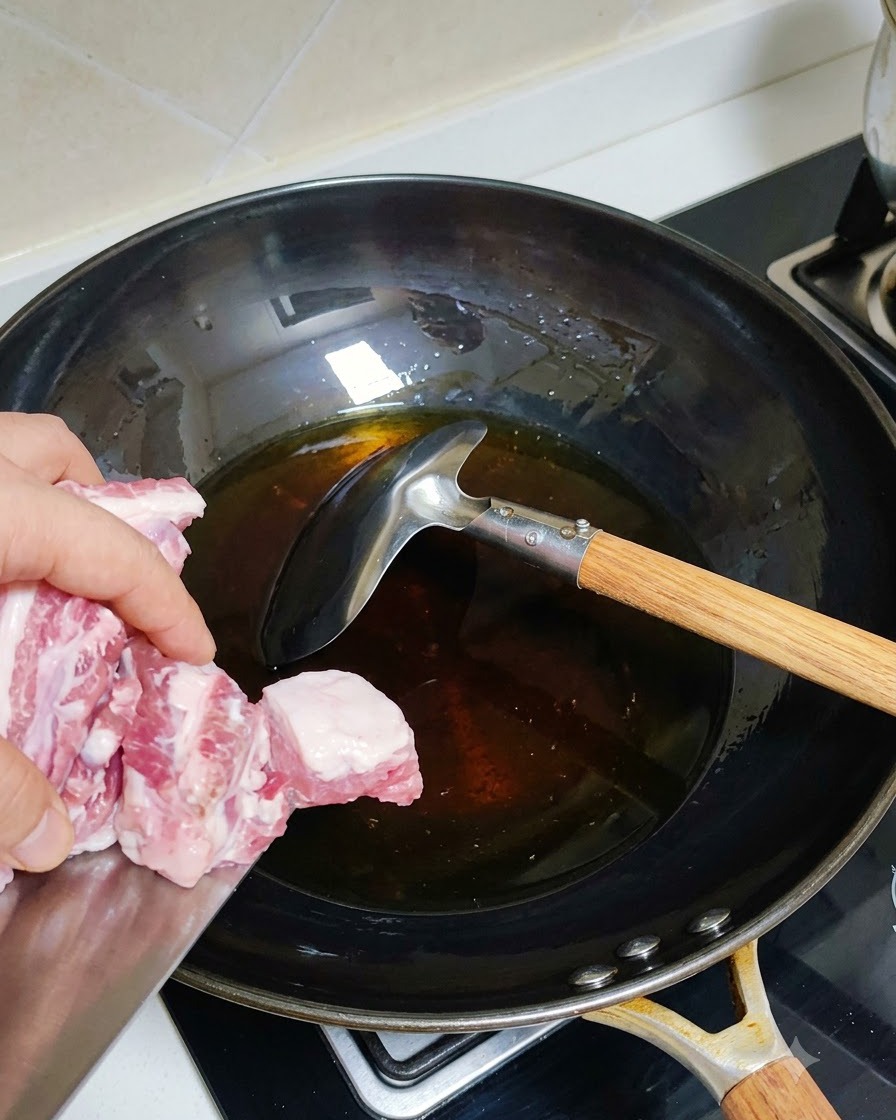 Costine di maiale sbollentate aggiunte a un wok caldo con olio.