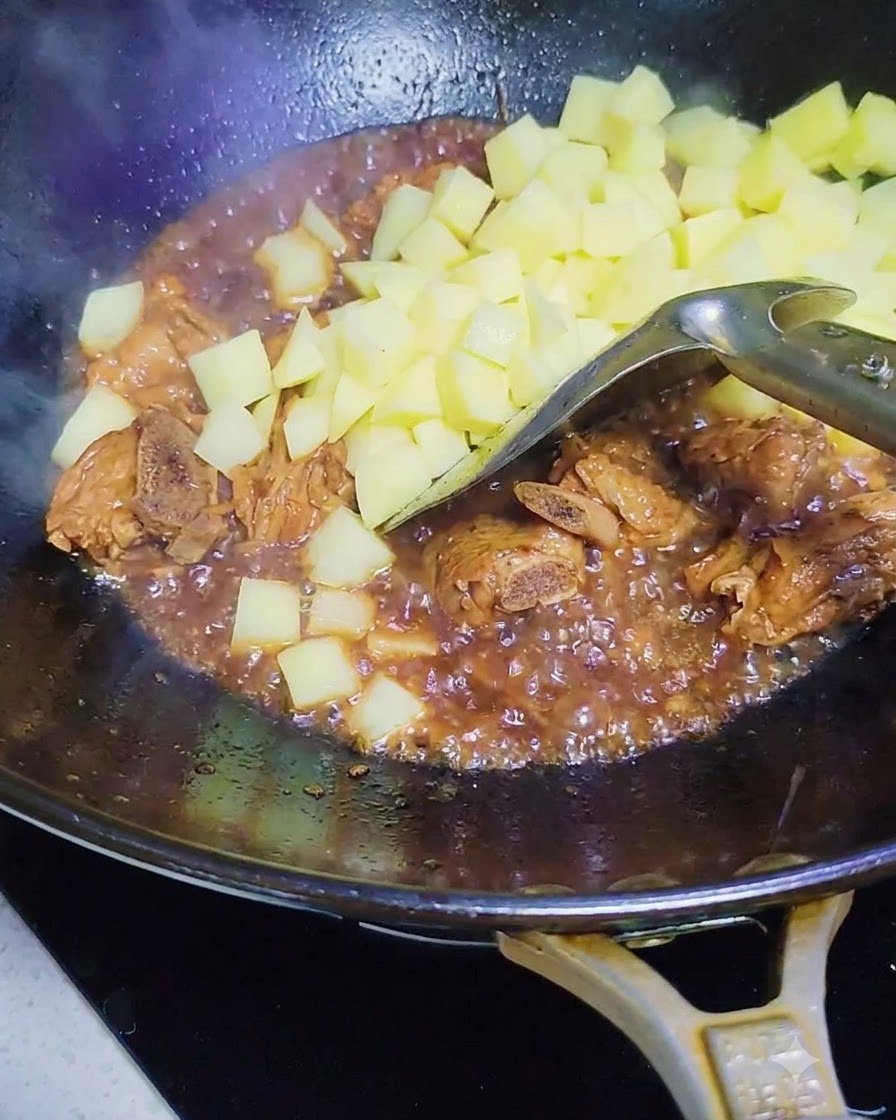 Patate crude a dadini aggiunte nel wok con le costine di maiale e la salsa.