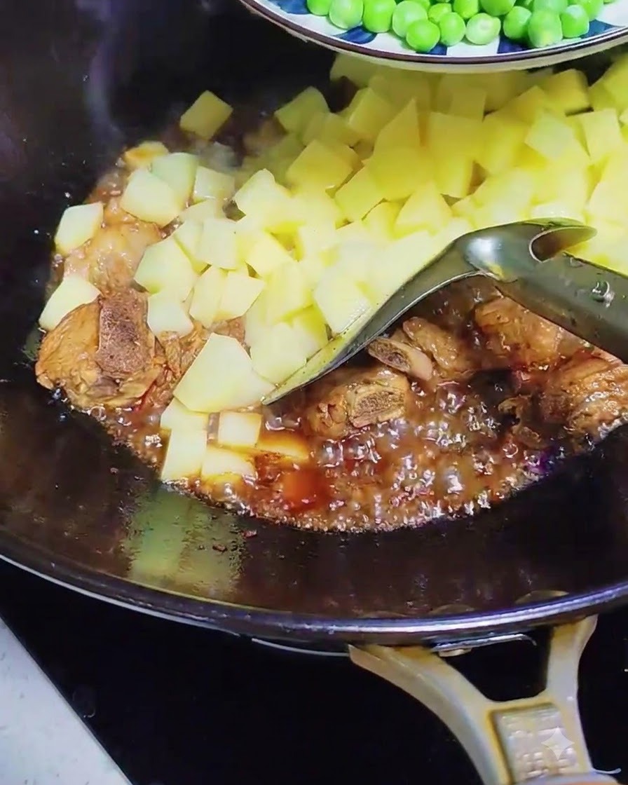 Piselli e fette di salsiccia aggiunti nel wok con costine di maiale e patate bollenti.