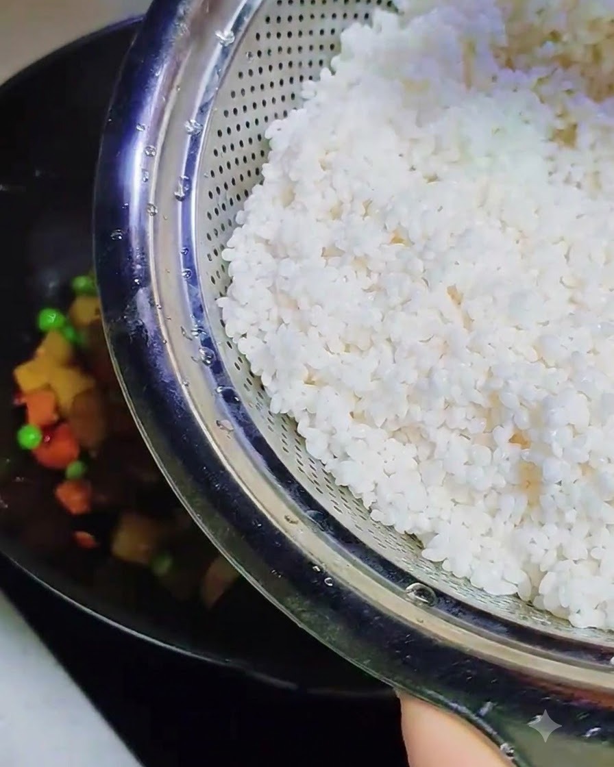 Riso glutinoso bagnato e morbido versato da un colino di metallo nel wok contenente gli altri ingredienti cotti.