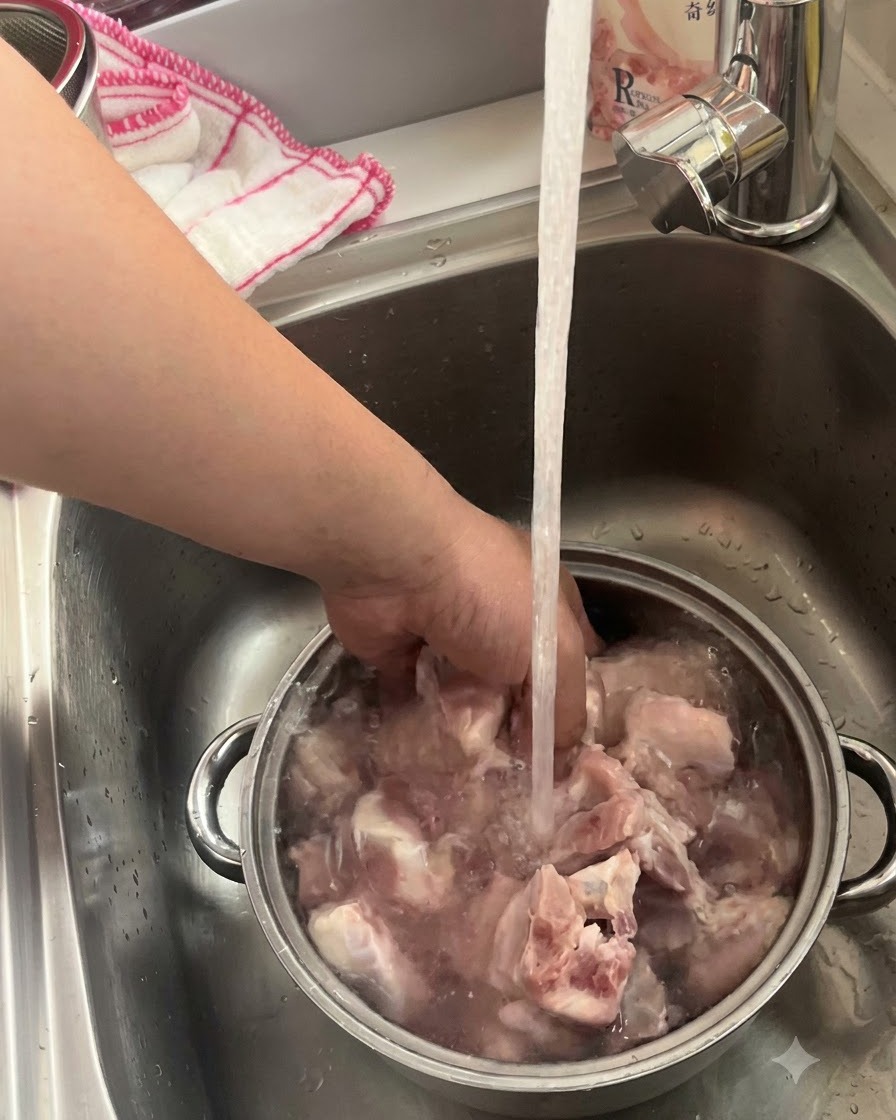 Costine di maiale in ammollo e lavate in una ciotola di metallo sotto lacqua corrente del rubinetto della cucina.