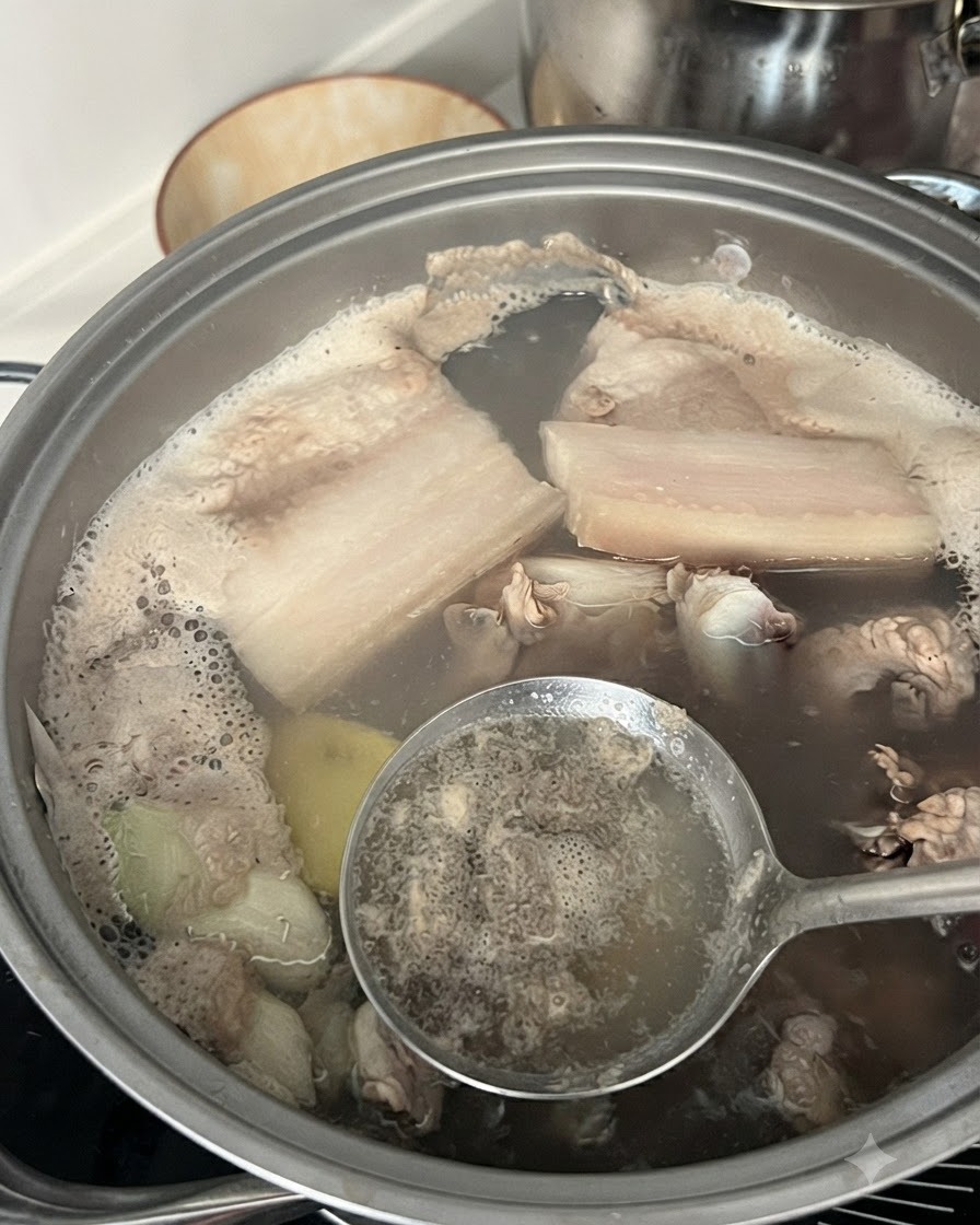 Un cucchiaio forato che rimuove la schiuma grigia e le impurità dallacqua bollente in una pentola contenente costine di maiale.