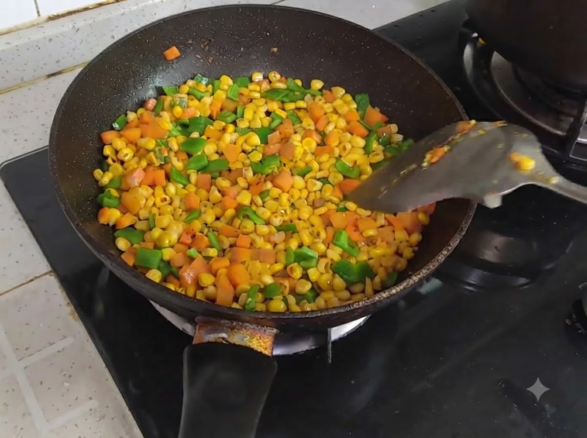 Una padella riempita con mais, carote e peperoni verdi a dadini saltati e mescolati con una spatola.