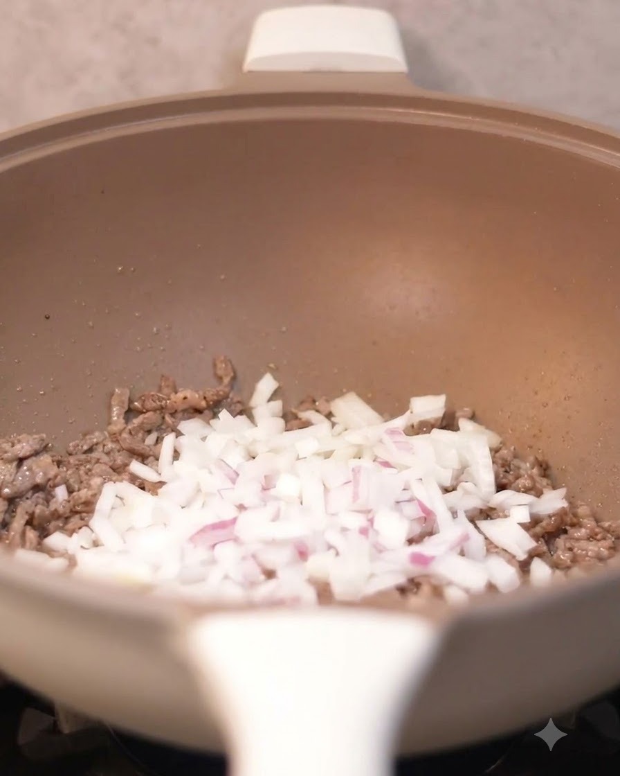 Cipolle a dadini versate nel wok con i pezzi di manzo cotto.