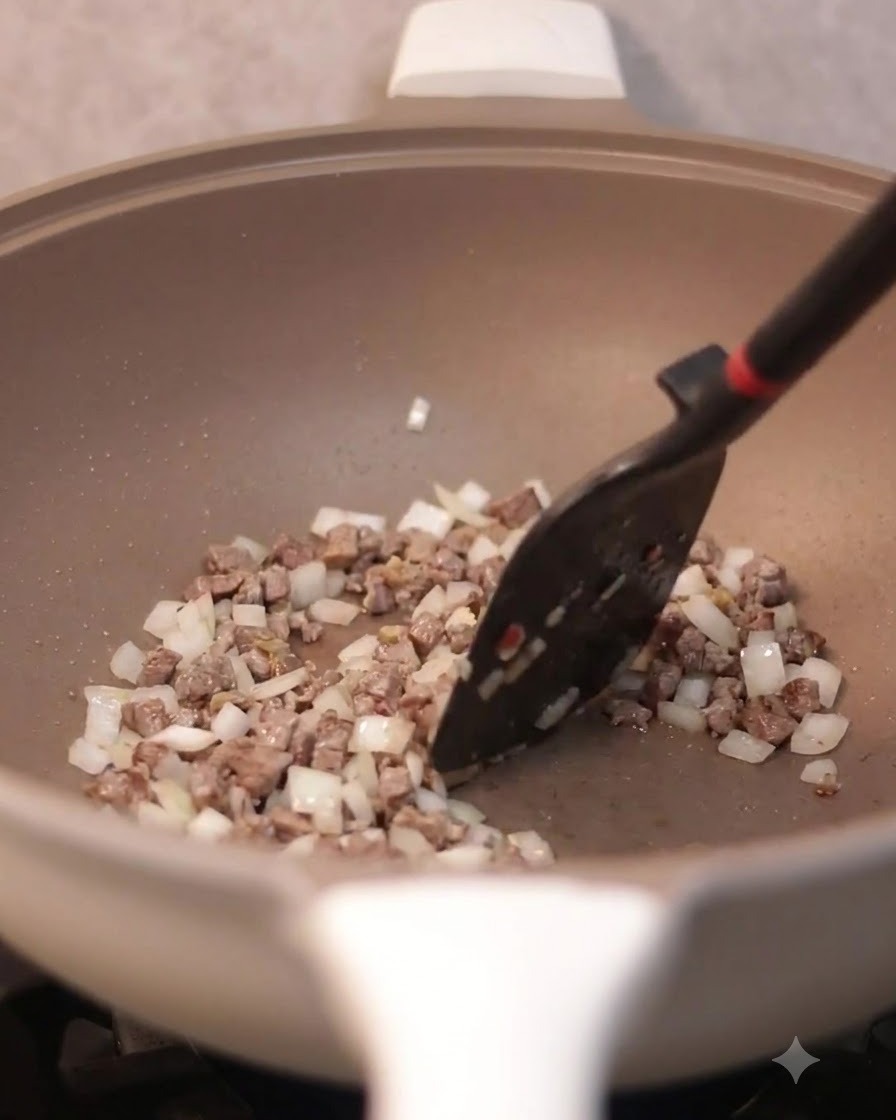 Una spatola che mescola uova strapazzate combinate con manzo e cipolle in padella.