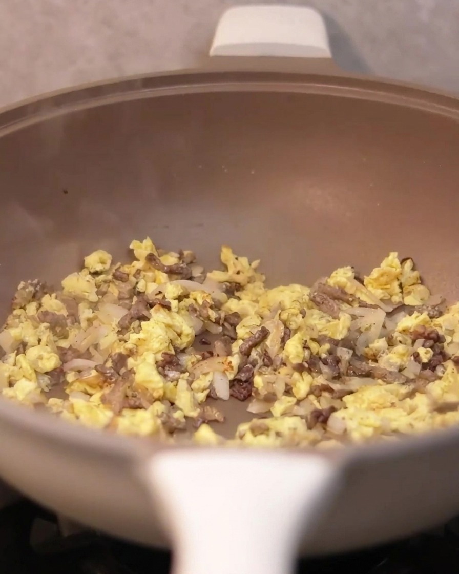 Salsa di tartufo versata con un cucchiaio nella padella contenente manzo, cipolle e uova.