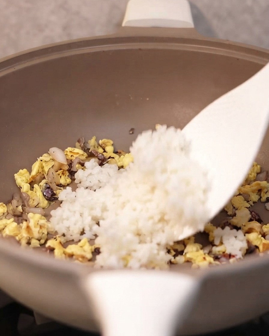 Una spatola che aggiunge riso bianco cotto nella padella con gli ingredienti conditi.