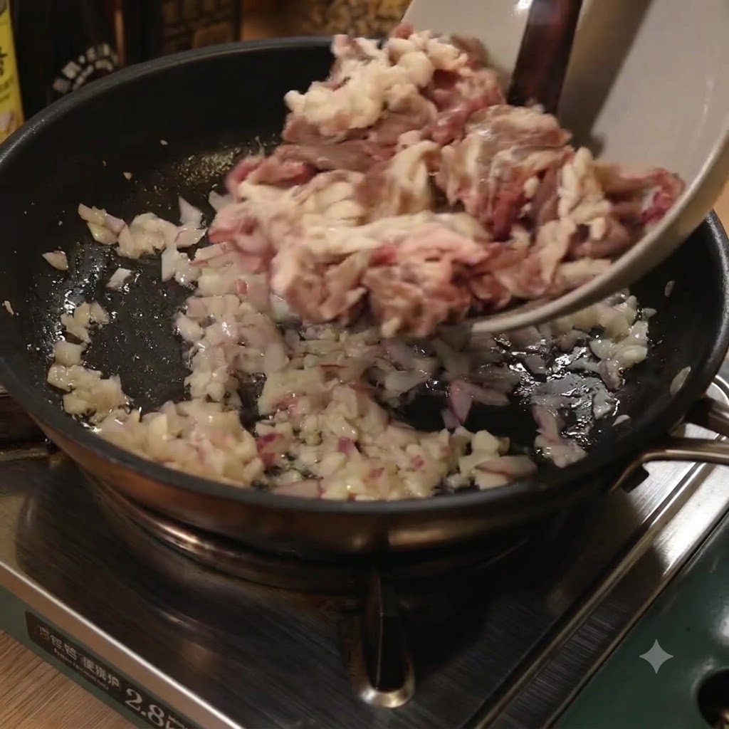 Strisce sottili di manzo aggiunte da una ciotola in una padella con cipolle e aglio.