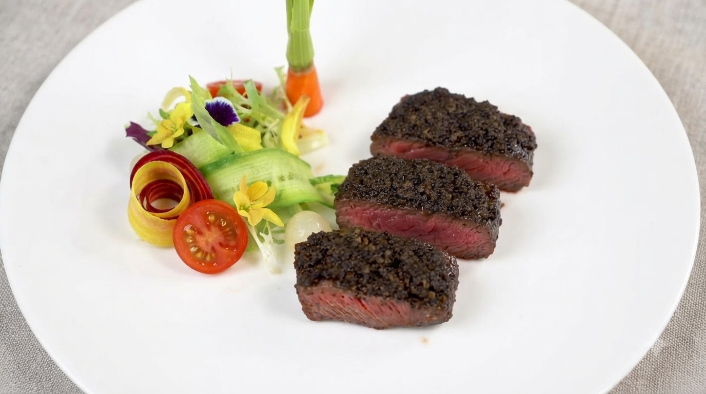 Tre fette spesse di bistecca cotta al sangue guarnite con ricca pasta di tartufo nero, servite insieme a contorni di verdure fresche.