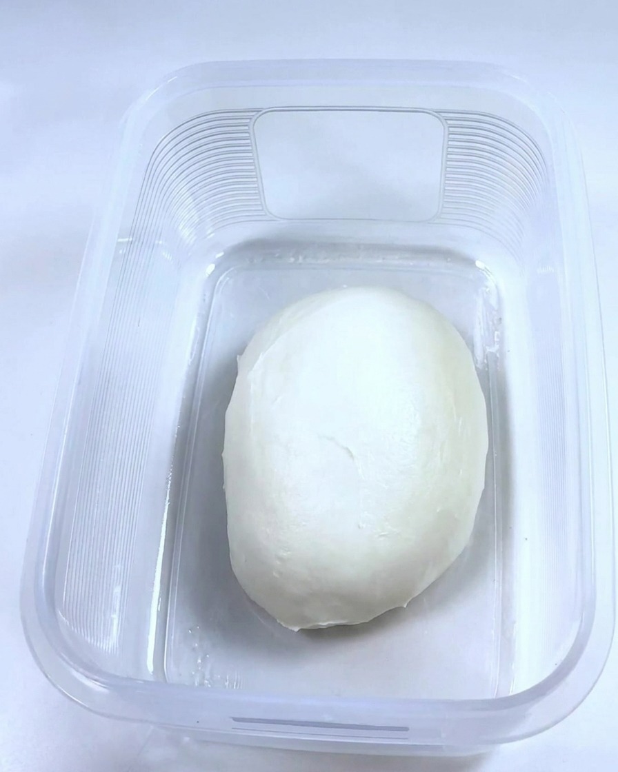 Una palla di impasto liscia che riposa allinterno di un contenitore di plastica rettangolare pulito e oliato.