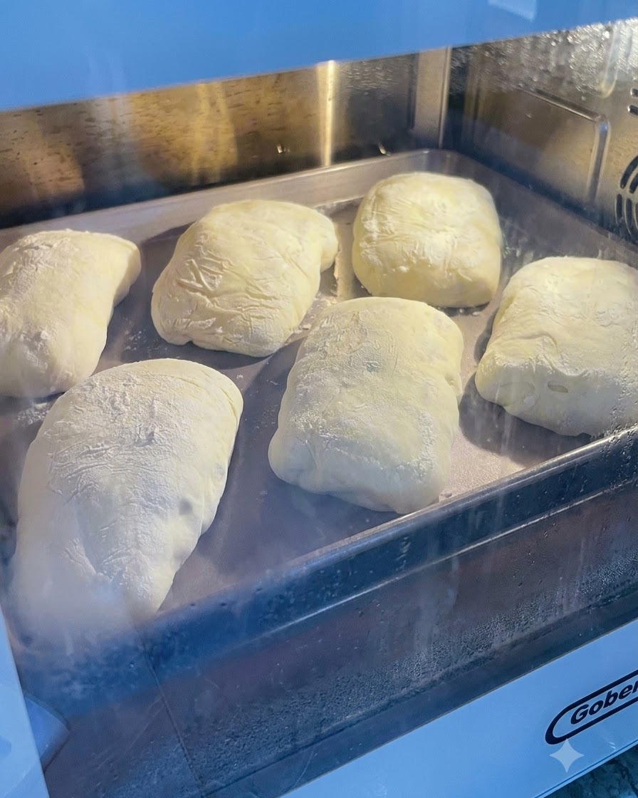 Impasto fermentato spolverato di farina adagiato su una teglia di metallo allinterno di un forno o di unarea di lievitazione.
