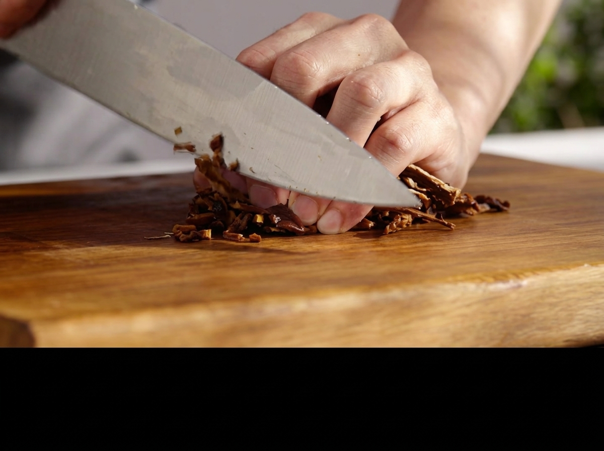 Un coltello che taglia finemente i funghi reidratati su un tagliere di legno.