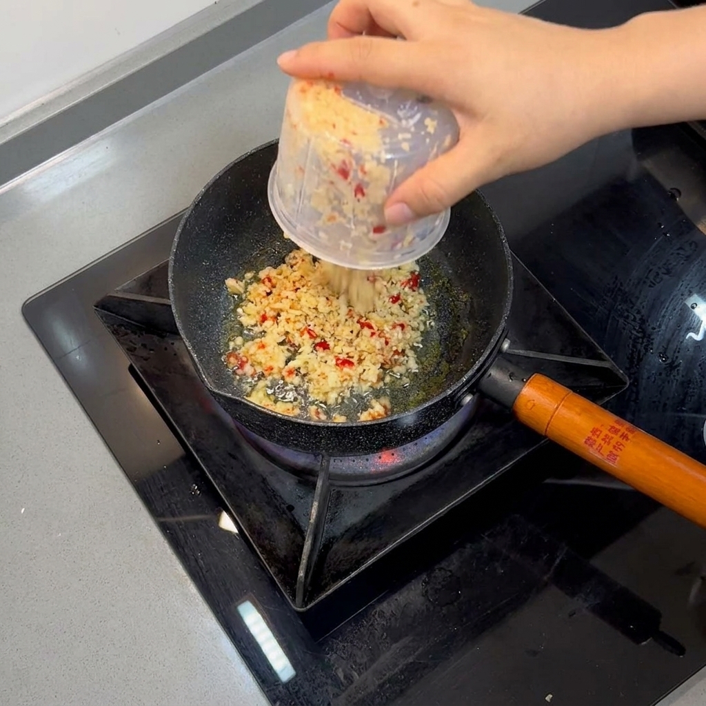 Aglio tritato e peperoncini rossi che soffriggono nellolio caldo allinterno di una piccola padella.