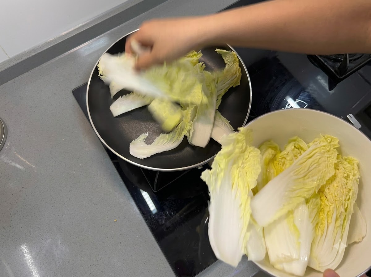 Foglie di cavolo cinese disposte a formare uno strato di base sul fondo di una padella.