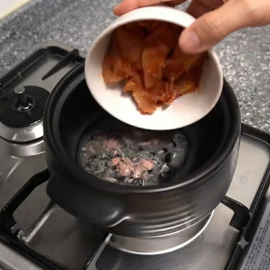 Una ciotola bianca che inclina e versa pezzi di kimchi rosso nella pentola di terracotta nera.