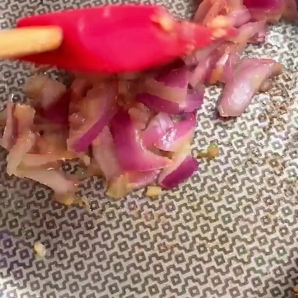 Spatola rossa che mescola attivamente gli ingredienti allinterno della padella.