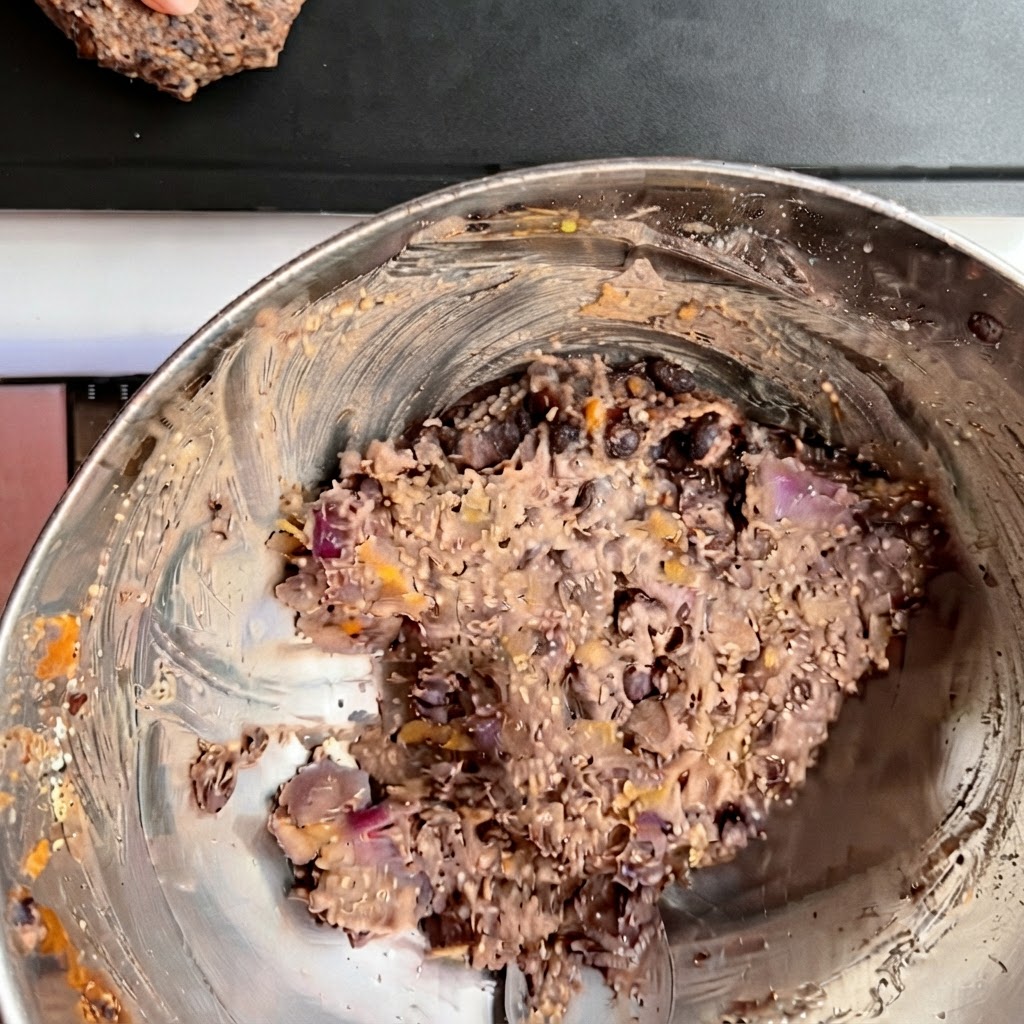 Diversi burger di fagioli neri modellati disposti ordinatamente su una teglia scura da forno.
