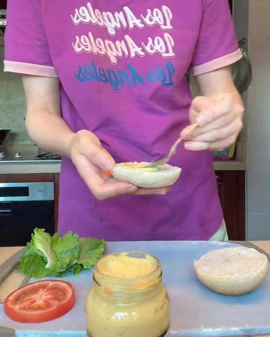 Mani che indossano guanti protettivi mentre modellano medaglioni di hamburger rotondi su un vassoio.