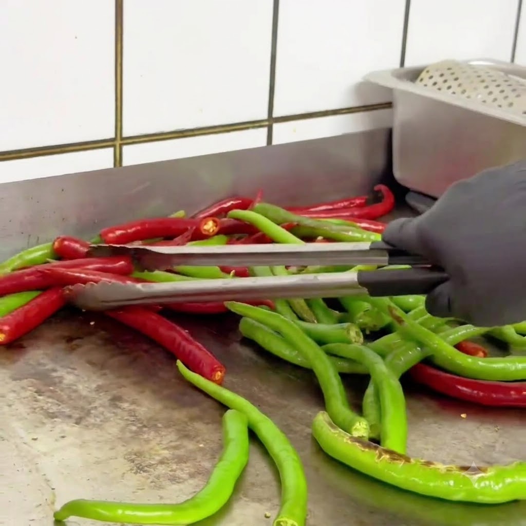 Peperoncini verdi e rossi girati con le pinze in una padella calda mentre si scuriscono.