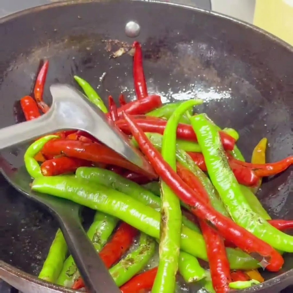 Peperoncini vescicati saltati con una spatola in un wok pieno di olio speziato luccicante.