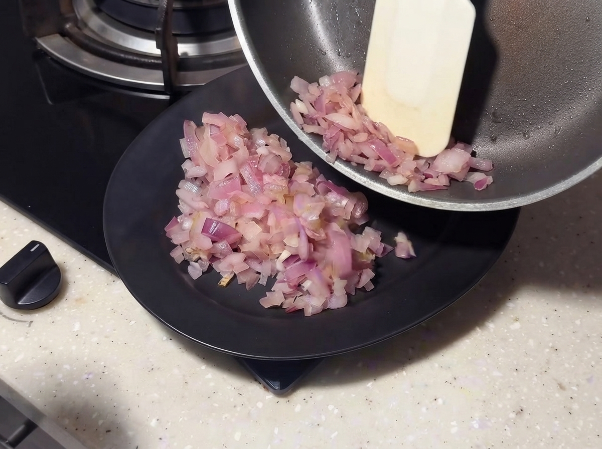 Cipolle saltate fatte scivolare da una padella su un piatto nero usando una spatola.