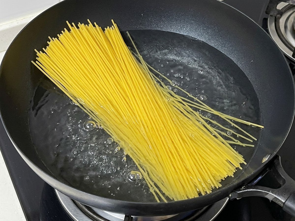 Un mazzetto di spaghetti secchi immersi in una pentola di acqua bollente.