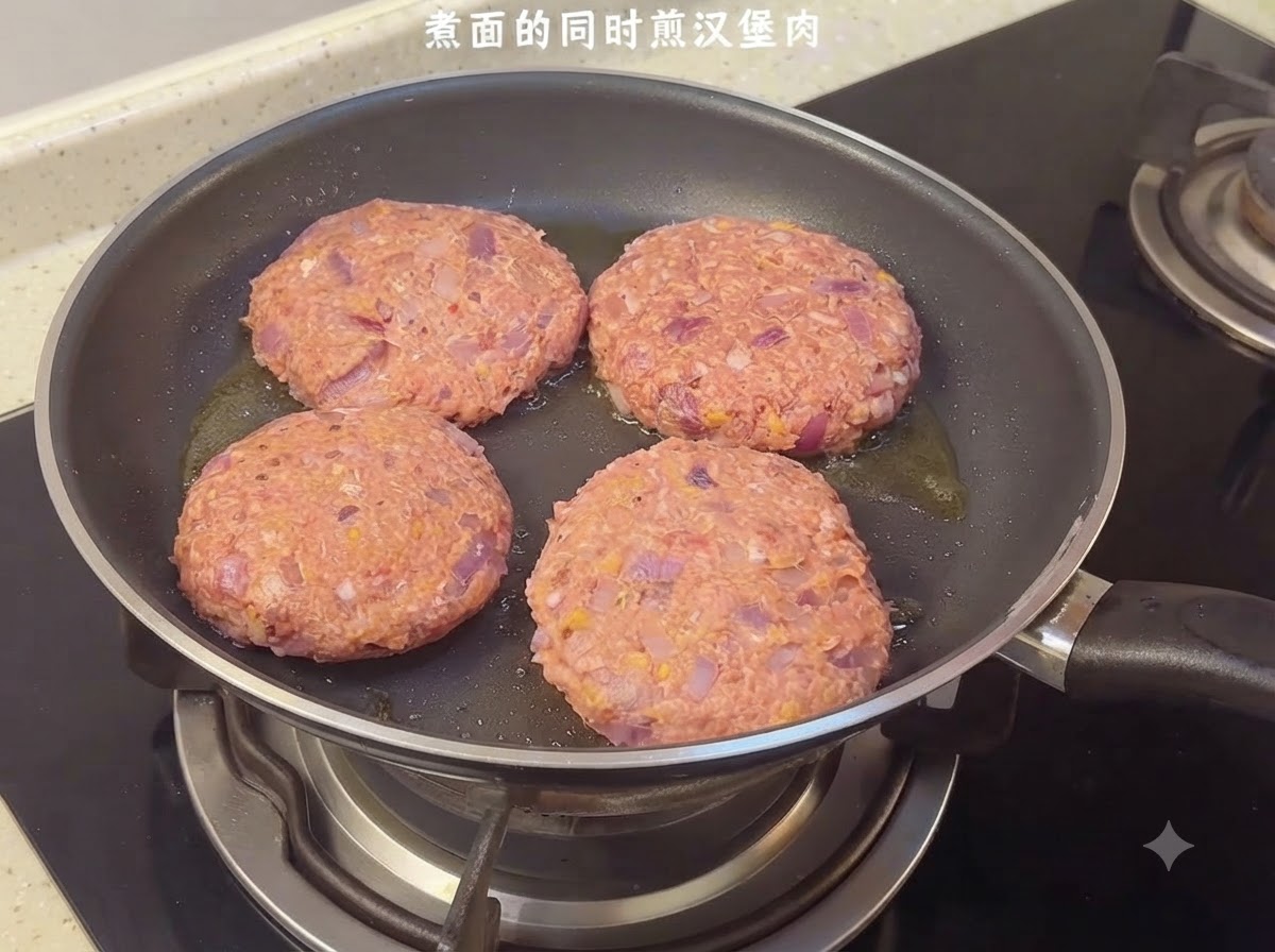 Quattro hamburger crudi che sfrigolano in una padella sul piano cottura.