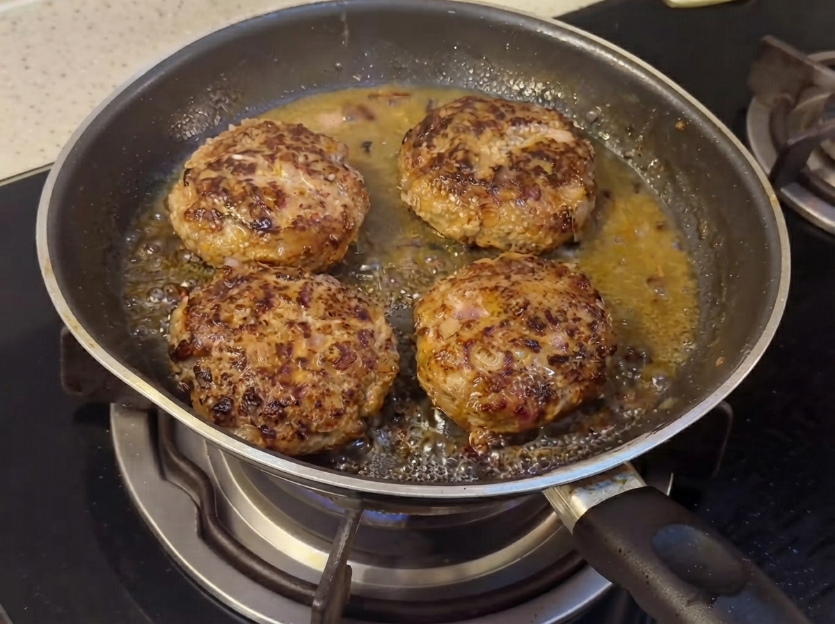 Hamburger che cuociono in padella con ingredienti liquidi della salsa che iniziano ad amalgamarsi.