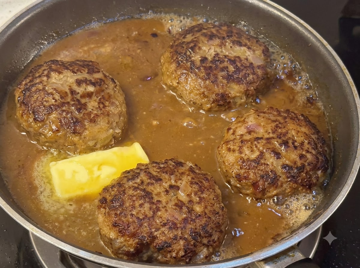 Hamburger che sobbollono in una densa salsa marrone accanto a un pezzo di burro che si scioglie.