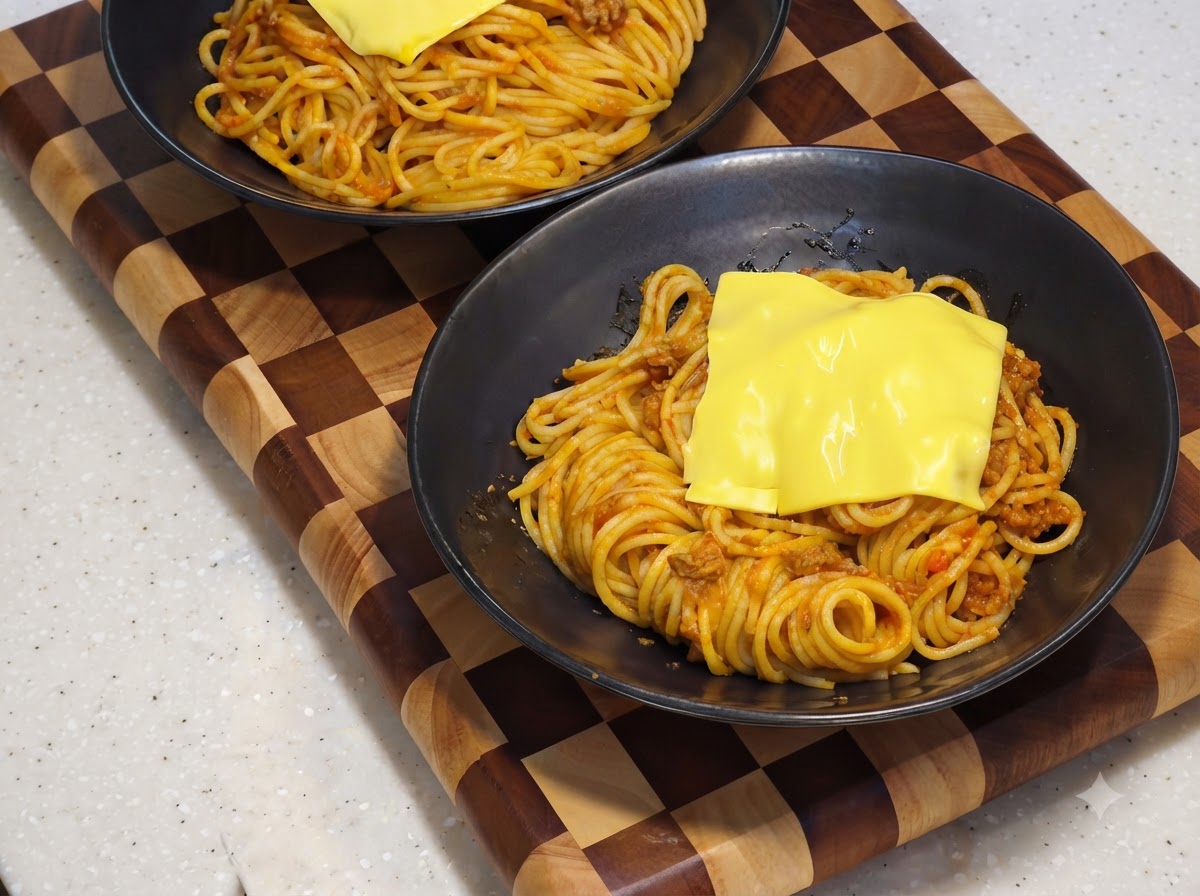 Una fetta di formaggio giallo che si scioglie sopra la base di spaghetti allinterno di una ciotola da portata nera.