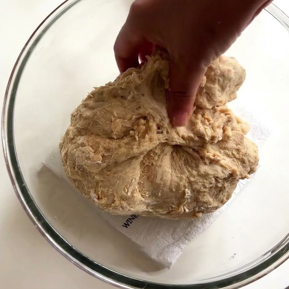 La mano di una persona che usa le dita bagnate per allungare e tirare limpasto appiccicoso allinterno di una ciotola di vetro.