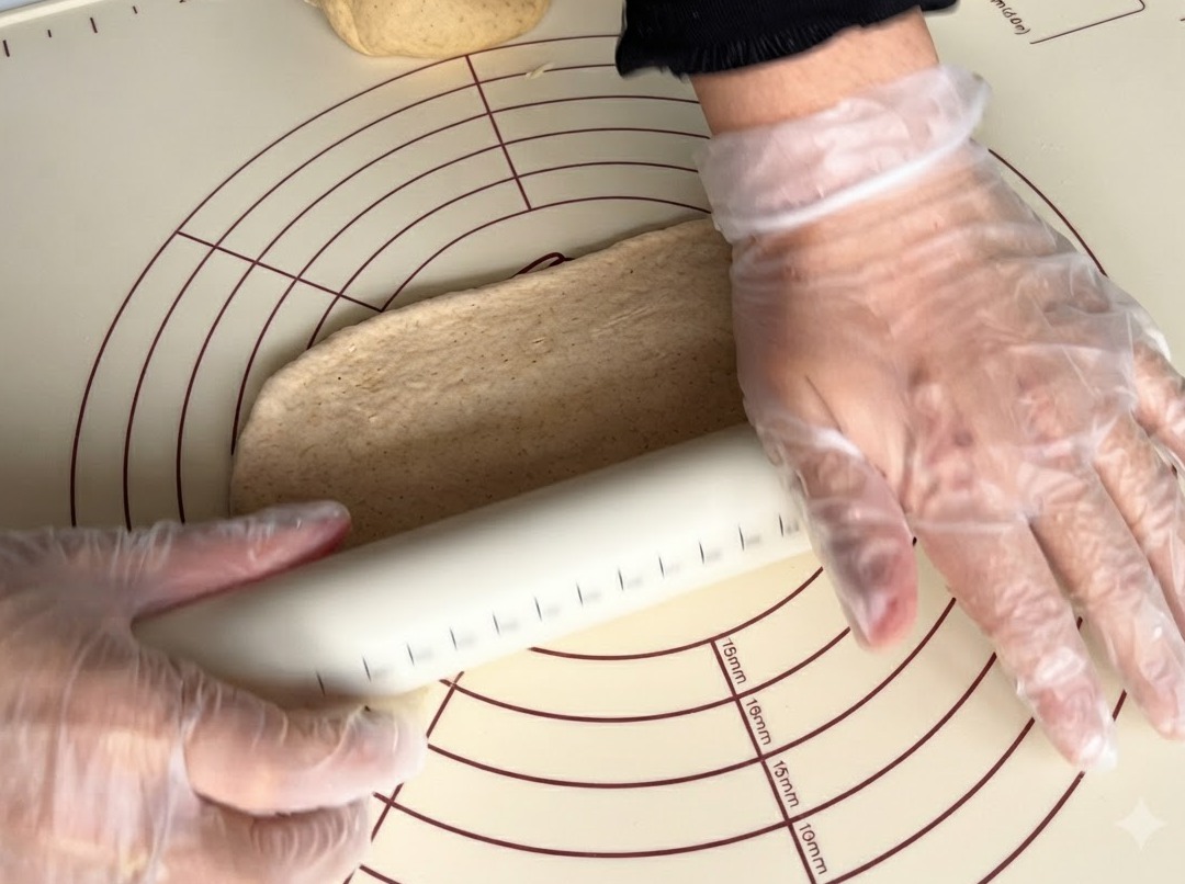 Un mattarello che appiattisce un pezzo di impasto integrale su un tappetino in silicone.