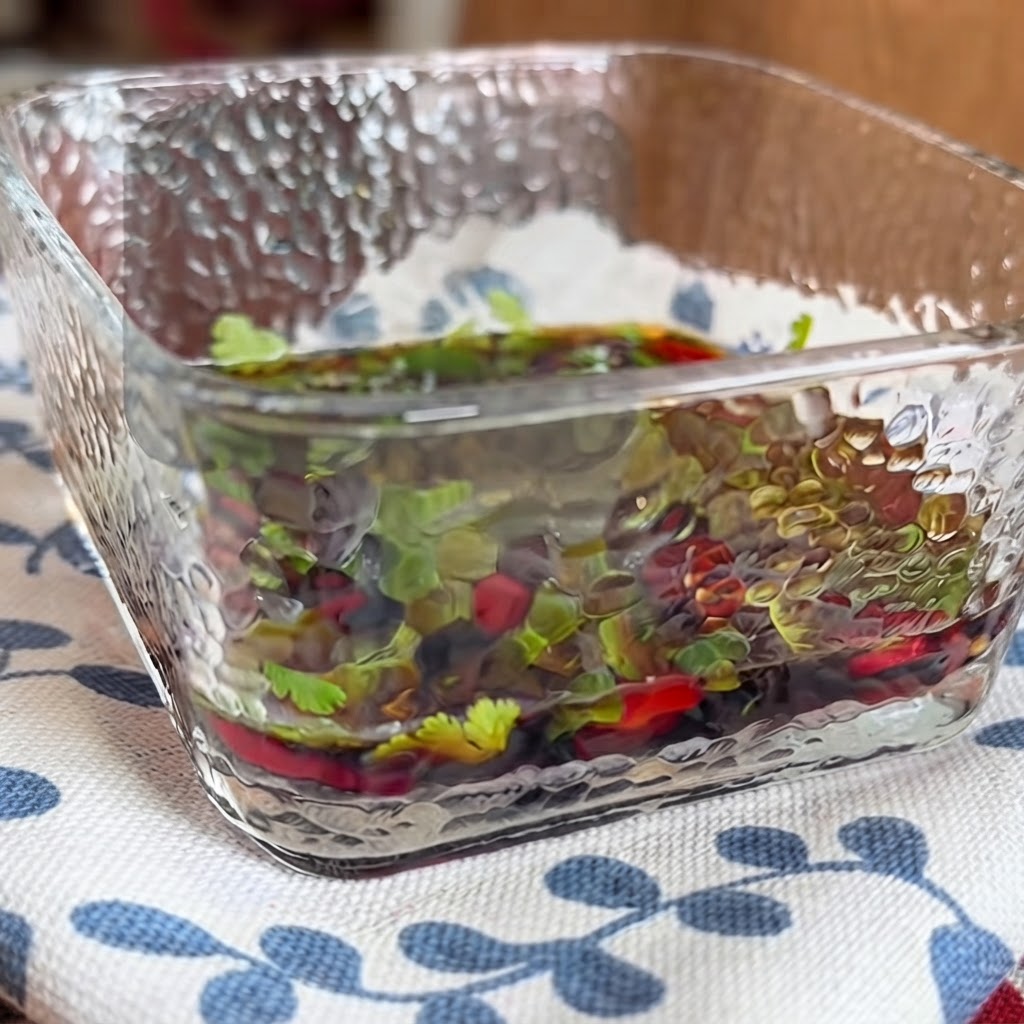 Primo piano di una ciototola di vetro quadrata riempita con una salsa saporita contenente erbe e peperoncini mescolata con le bacchette.