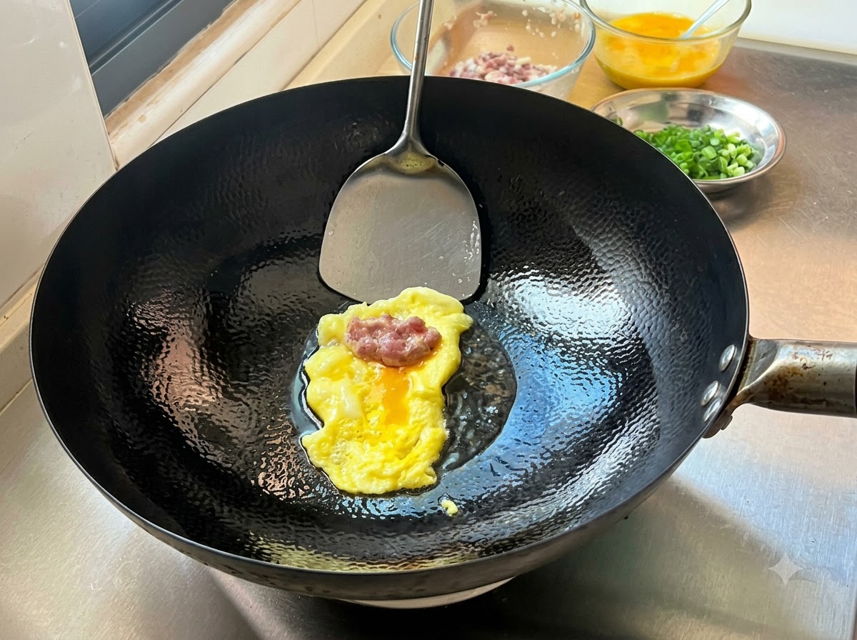 Una porzione di ripieno di carne condita adagiata su una crêpes di uova sottile appena cotta in un wok caldo, pronta per essere piegata.