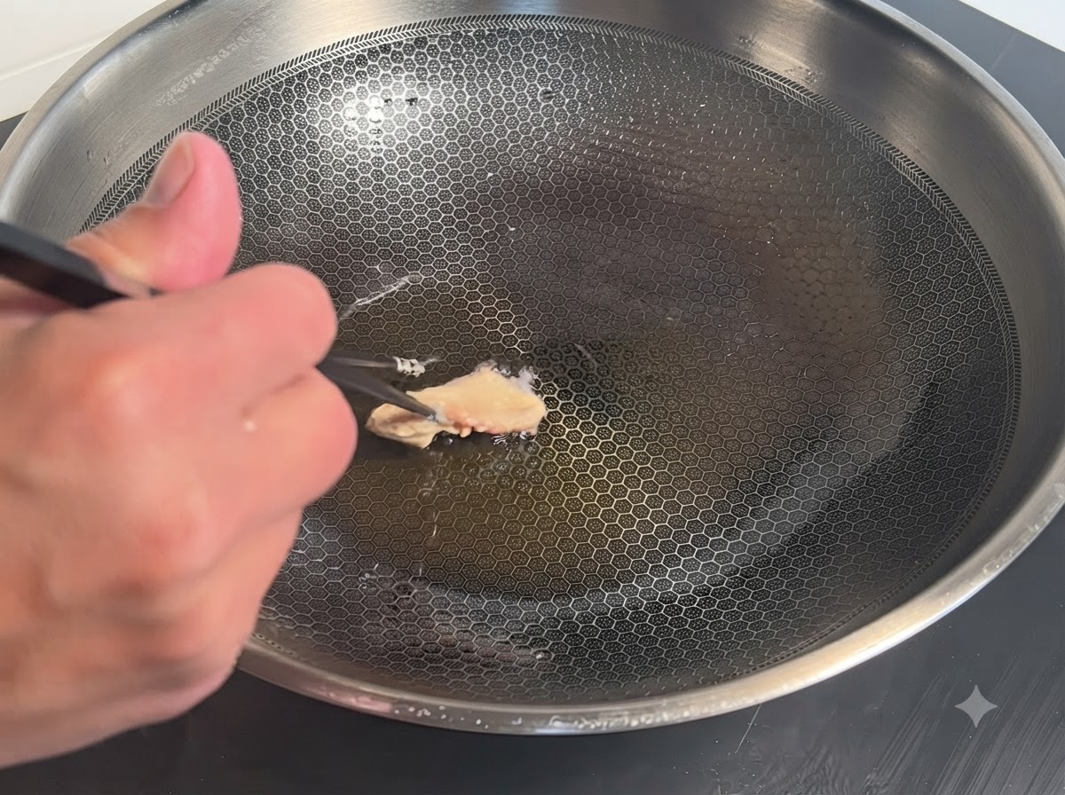 Un singolo pezzo di pollo rivestito di pastella posizionato con le bacchette in un wok di metallo caldo con olio.
