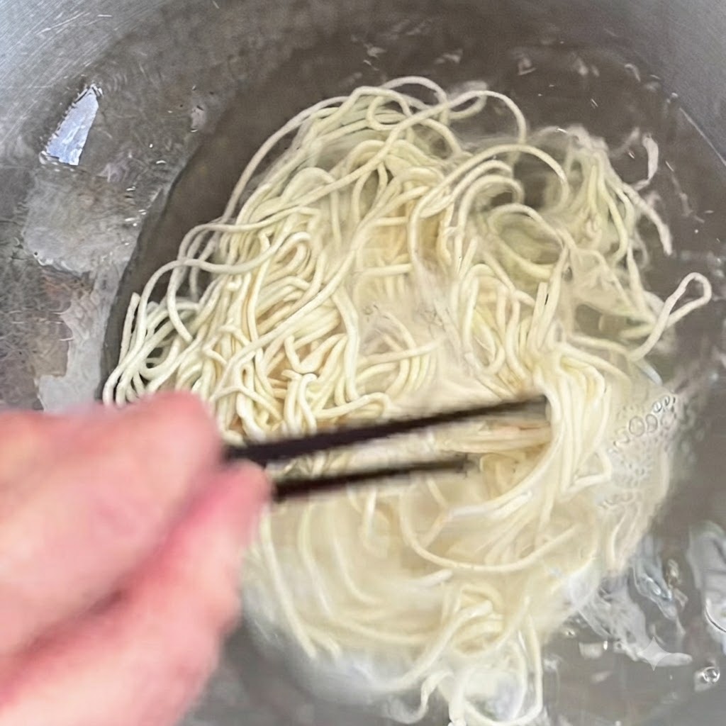 Noodles in cottura in una pentola mescolati con le bacchette.