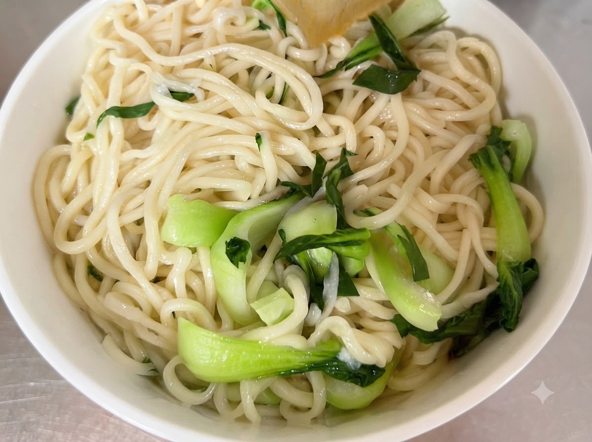 Noodles cotti e bok choy fresco disposti allinterno di una ciotola da portata bianca.