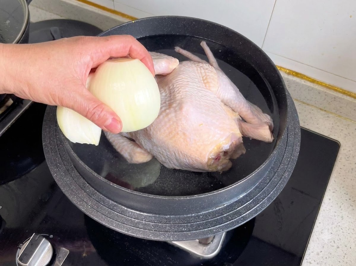 Mezza cipolla e altri aromi vengono gettati in una pentola contenente un pollo intero e acqua.
