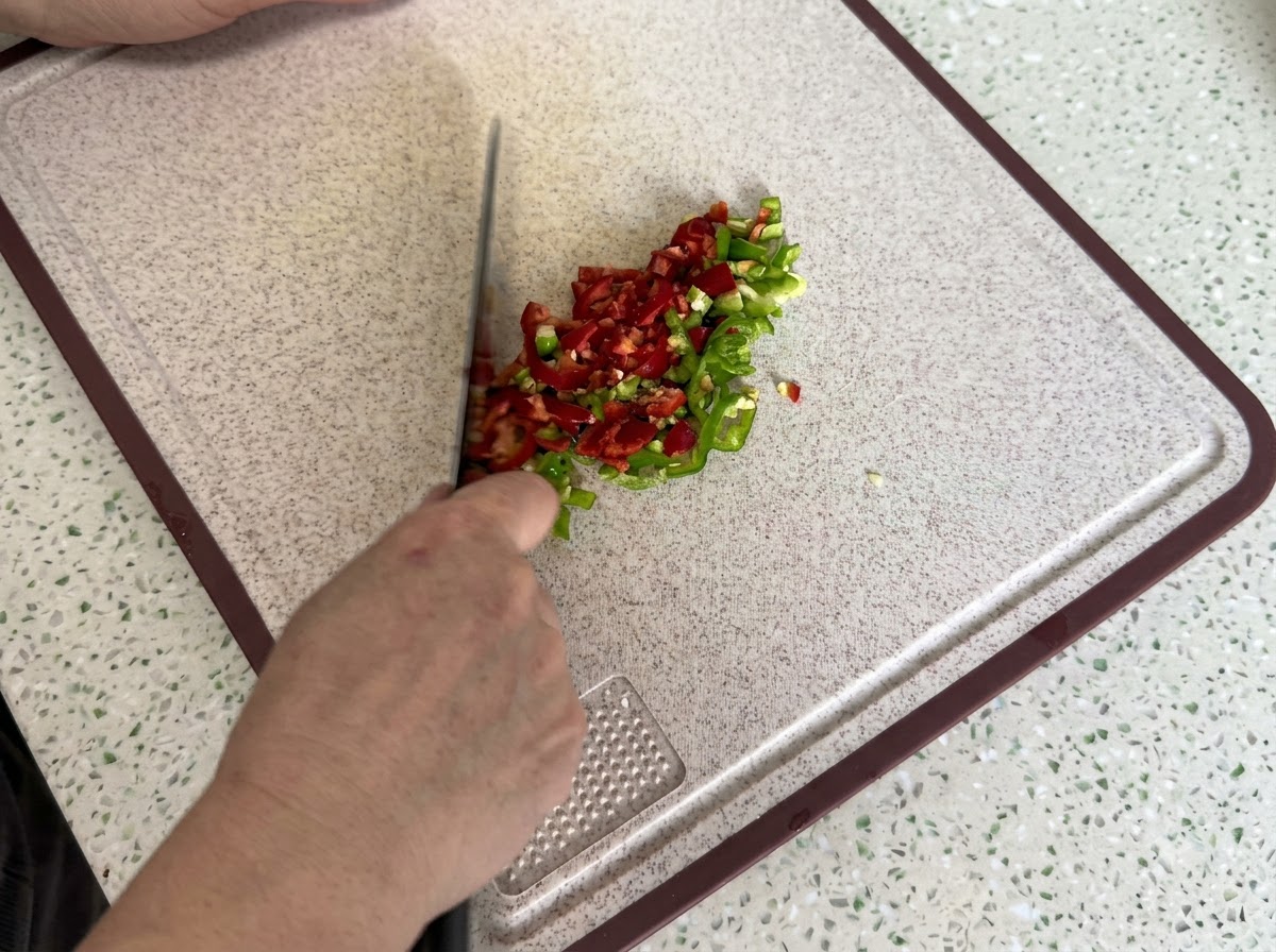 Peperoncini rossi e verdi finemente affettati e tagliati a cubetti su un tagliere pulito.