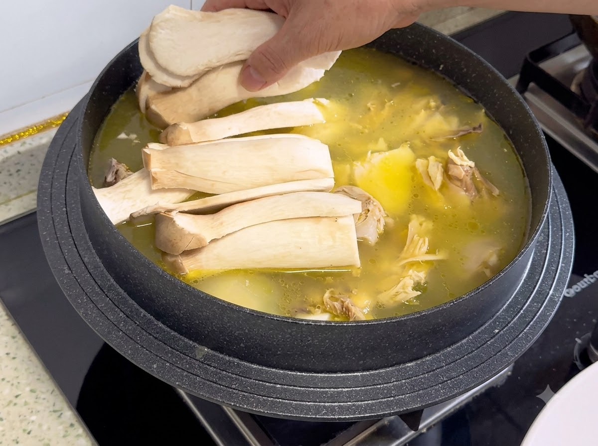 Funghi cardoncelli affettati disposti sopra il brodo di pollo e gli ingredienti in una pentola.