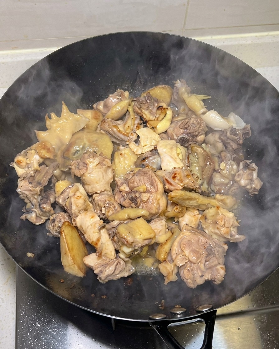 Pezzi di pollo dorati e scottati in cottura in un wok con vapore che sale.