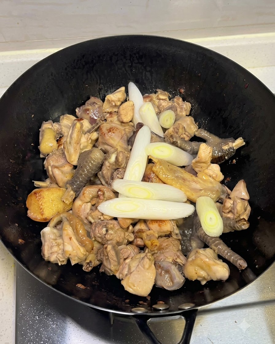 Aggiunta di cipollotti, aglio e spezie intere nel wok con il pollo.