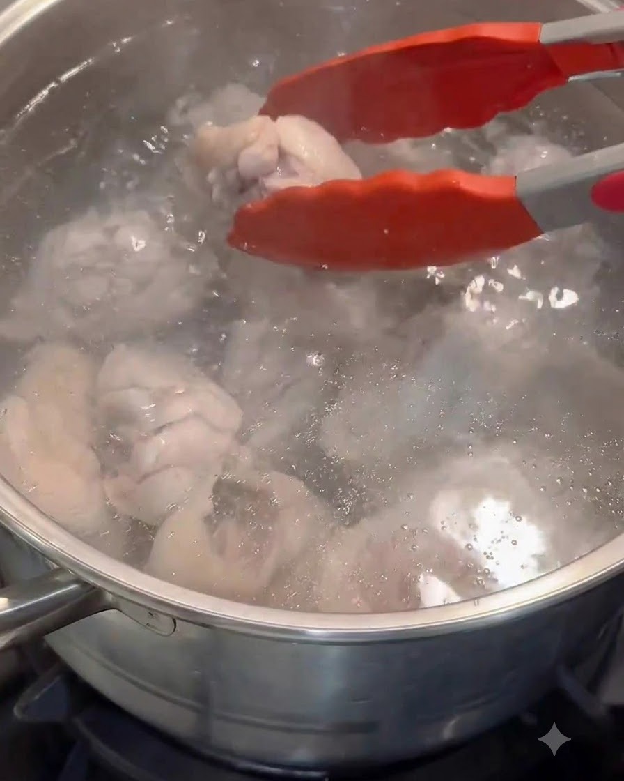 Pinze rosse trasferiscono i pezzi di pollo sbollentati in una pentola di acqua calda pulita.
