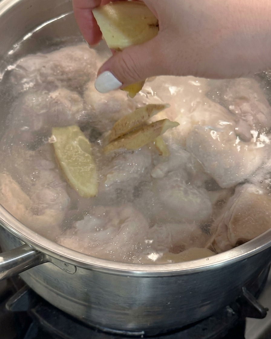 Una mano getta fette di zenzero fresco in una pentola di acqua bollente con il pollo.