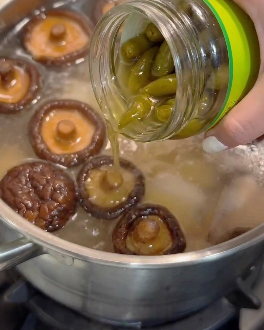 Succo di peperoncino sottaceto pelato versato da un barattolo di vetro in una pentola di zuppa sobbollente con funghi shiitake.