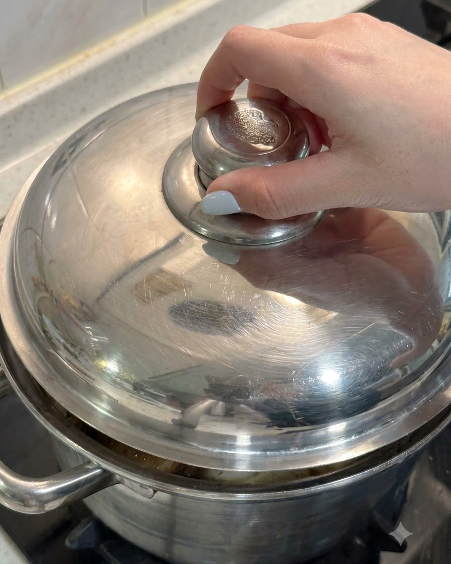 Una mano posiziona il coperchio di metallo su una pentola piena di pollo e ingredienti per la zuppa.